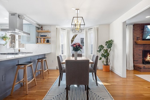 dining room featuring light wood-type flooring, a brick fireplace, baseboards, and a chandelier