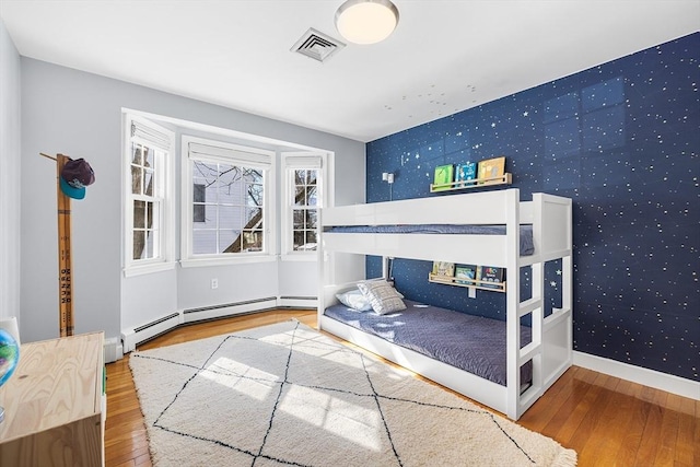 bedroom featuring an accent wall, wood finished floors, visible vents, and wallpapered walls