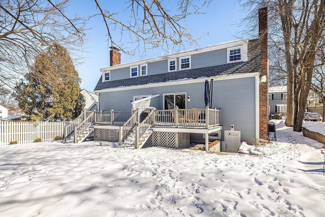 snow covered rear of property with a deck, fence, stairs, roof with shingles, and a chimney