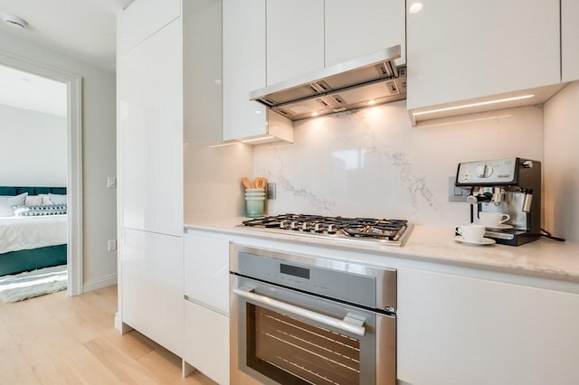 kitchen with modern cabinets, light countertops, under cabinet range hood, white cabinets, and appliances with stainless steel finishes