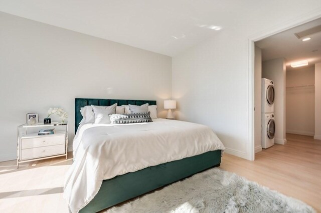 bedroom with baseboards, stacked washer / drying machine, wood finished floors, and lofted ceiling