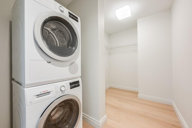 laundry area with baseboards, stacked washer and dryer, wood finished floors, and laundry area