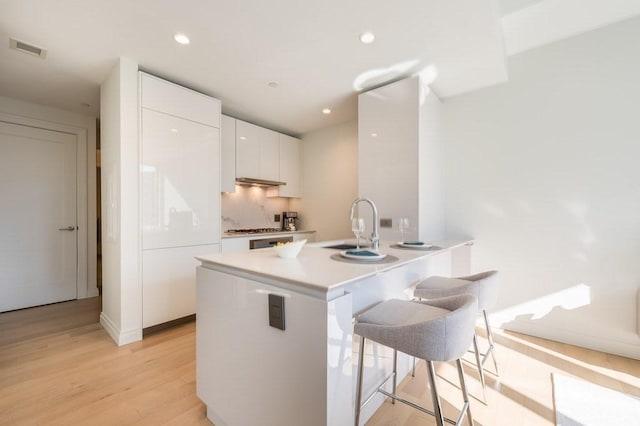 kitchen with white cabinets, a breakfast bar, a sink, light wood-style flooring, and visible vents
