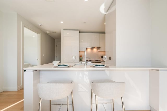 kitchen featuring modern cabinets, a kitchen bar, white cabinets, a sink, and light wood finished floors