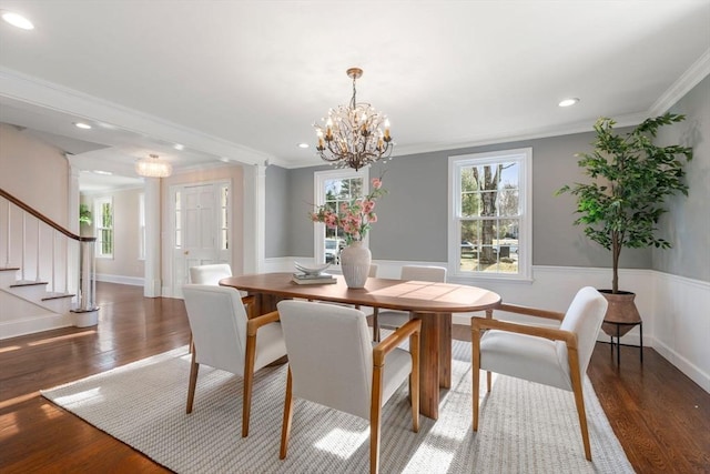 dining space featuring a wainscoted wall, a notable chandelier, wood finished floors, stairs, and ornate columns