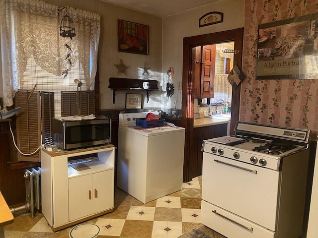 kitchen featuring stainless steel microwave, washer / clothes dryer, light floors, radiator, and white range with gas stovetop