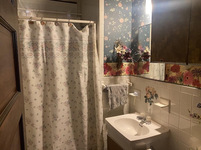 bathroom featuring wallpapered walls, a sink, wainscoting, curtained shower, and tile walls