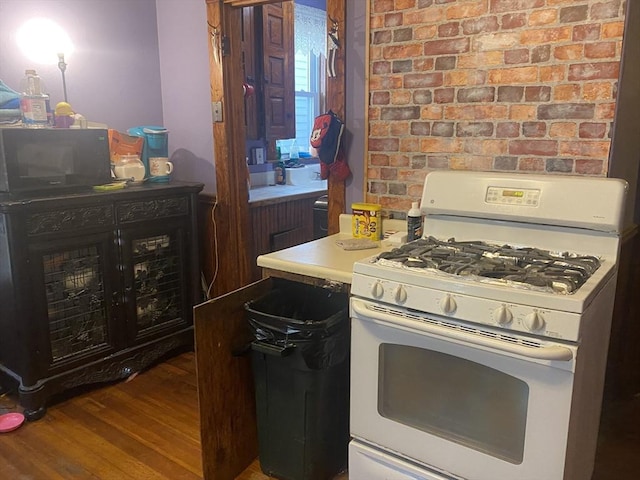 kitchen with wood finished floors, white gas range, and brick wall