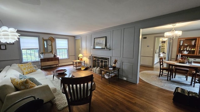 living room with a chandelier, crown molding, dark wood-style flooring, a glass covered fireplace, and a decorative wall