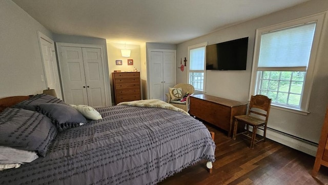 bedroom with baseboard heating, dark wood-style flooring, and multiple closets