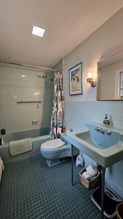 bathroom featuring tile walls, toilet, shower / bath combo with shower curtain, tile patterned flooring, and a wainscoted wall