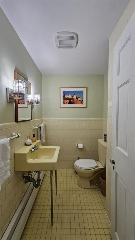 bathroom featuring tile walls, toilet, tile patterned floors, a wainscoted wall, and a sink