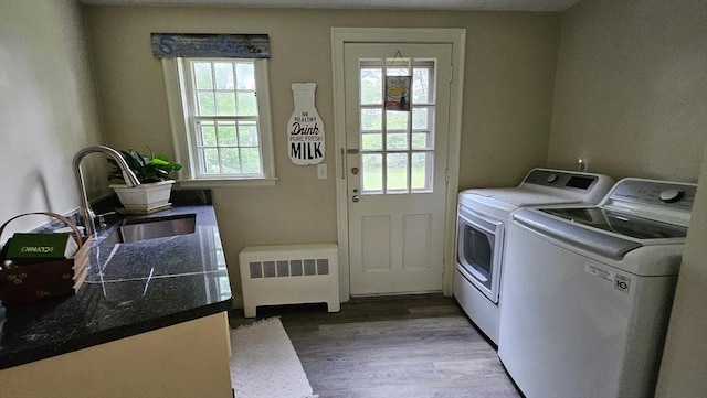 clothes washing area with radiator heating unit, washer and dryer, healthy amount of natural light, and wood finished floors