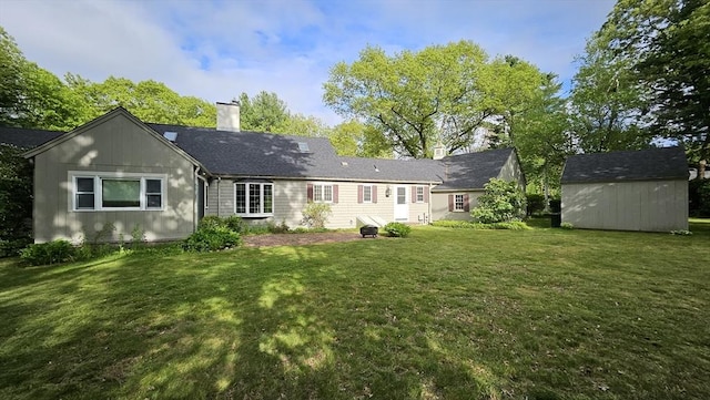 back of house with a chimney, a storage unit, an outdoor structure, and a yard