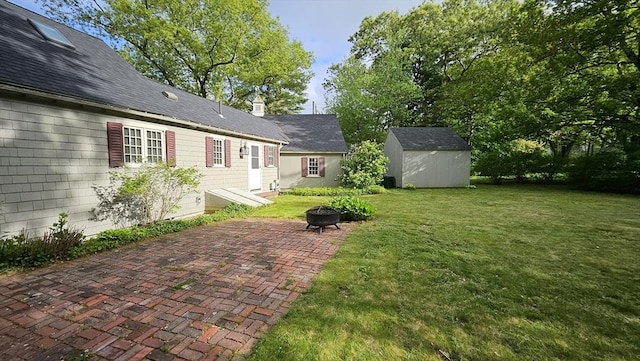 view of grassy yard featuring a storage shed, a patio area, an outbuilding, and a fire pit