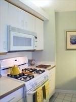 kitchen featuring white appliances, white cabinetry, and light tile patterned flooring