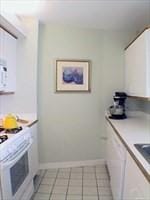 kitchen featuring white cabinets, light tile patterned flooring, and white stove