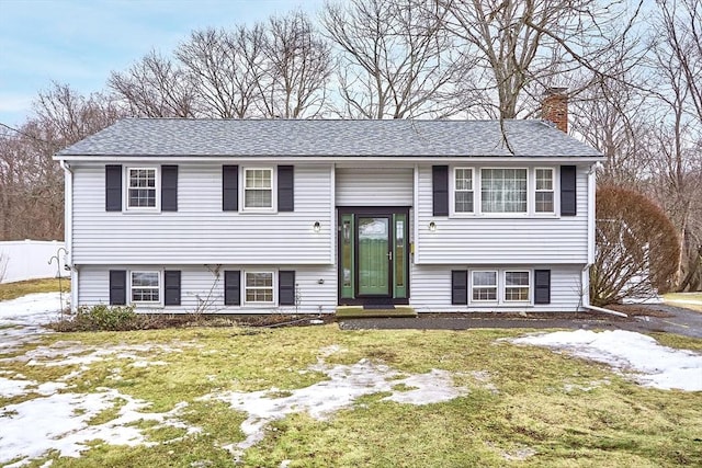 raised ranch featuring a shingled roof, fence, a chimney, and a front lawn