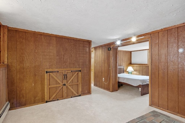 unfurnished bedroom with a baseboard heating unit, a textured ceiling, carpet flooring, and wooden walls