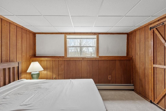 carpeted bedroom with a baseboard radiator, a drop ceiling, and wood walls