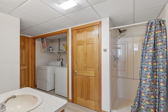 bathroom featuring a drop ceiling, independent washer and dryer, a shower stall, and a sink