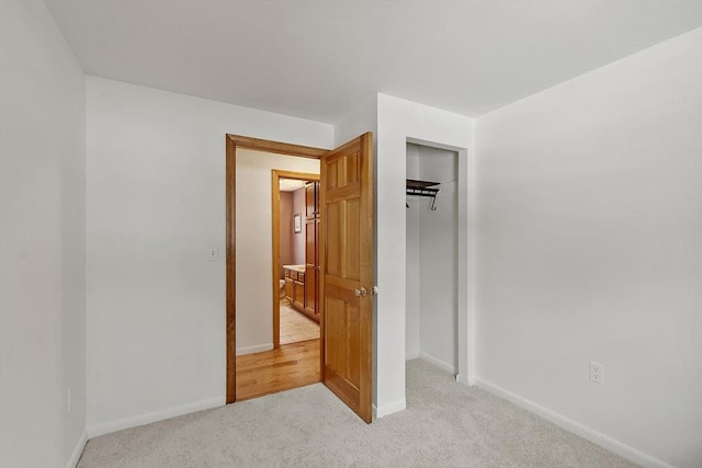 unfurnished bedroom with a closet, light carpet, and baseboards