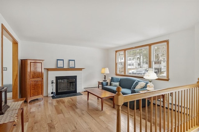 living area with a baseboard heating unit, light wood-type flooring, and a fireplace with flush hearth