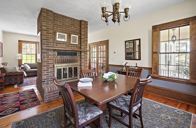 185 Woodland St, Natick, MA 01760 - dining space featuring wood-type flooring, a chandelier, a textured ceiling, and a fireplace