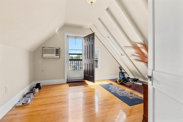 additional living space featuring lofted ceiling, a wall mounted air conditioner, baseboards, and hardwood / wood-style floors