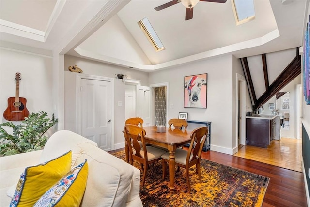 dining area with a ceiling fan, dark wood-style flooring, baseboards, and lofted ceiling with skylight