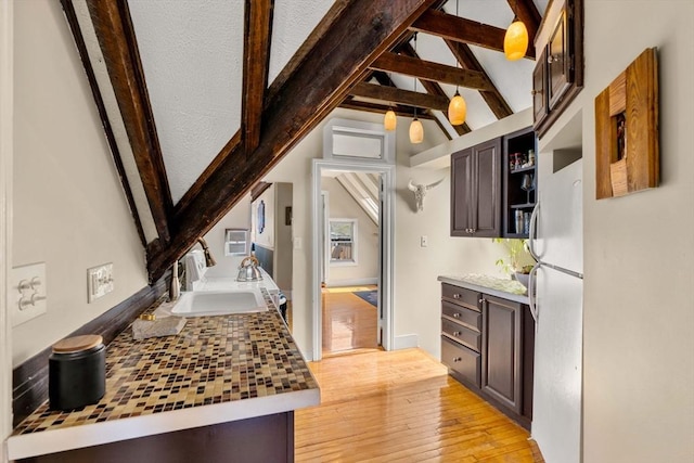kitchen with freestanding refrigerator, a sink, dark brown cabinetry, open shelves, and light wood-style floors
