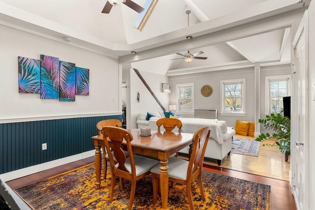 dining area featuring a ceiling fan, hardwood / wood-style floors, a wainscoted wall, and vaulted ceiling with beams