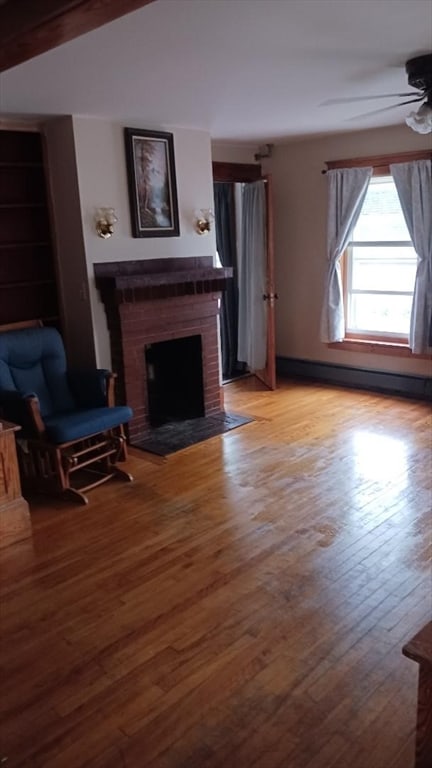 unfurnished living room with a baseboard radiator, a brick fireplace, ceiling fan, and light wood-type flooring