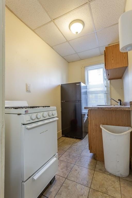 kitchen with light tile patterned flooring, a paneled ceiling, white range with gas cooktop, kitchen peninsula, and black fridge