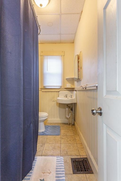 bathroom featuring a drop ceiling, tile patterned flooring, wooden walls, and toilet