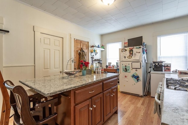 kitchen with white appliances, a kitchen breakfast bar, light stone countertops, a kitchen island, and light wood-type flooring