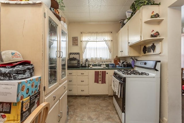 kitchen featuring white range with gas cooktop, sink, and white cabinets