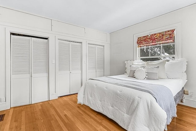 bedroom featuring wood finished floors, visible vents, and multiple closets