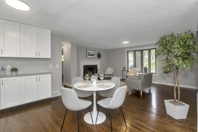 dining space featuring baseboards, dark wood-type flooring, a fireplace, and a textured ceiling