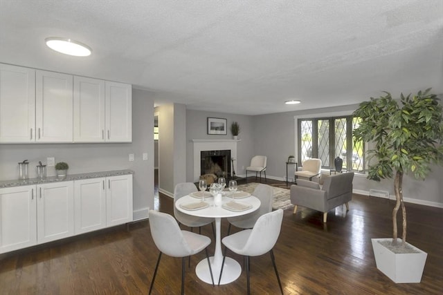 dining space featuring baseboards, a fireplace, dark wood-style floors, and a textured ceiling