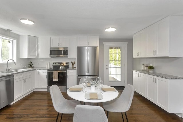 kitchen with stainless steel appliances, a sink, white cabinetry, light stone counters, and dark wood-style flooring