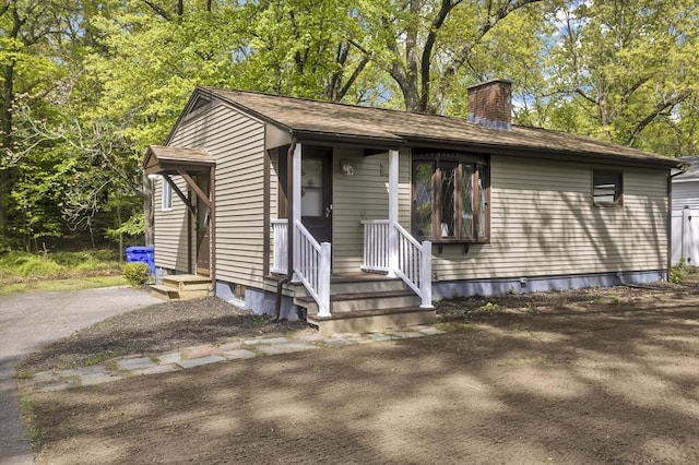 view of front of home with a chimney, entry steps, and view of wooded area