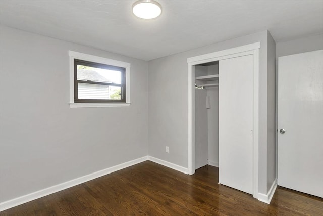 unfurnished bedroom featuring dark wood finished floors, a closet, and baseboards