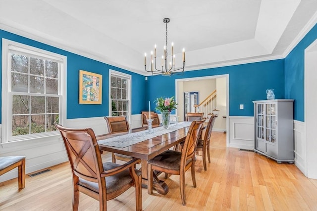 dining space with a notable chandelier, light wood-type flooring, and a raised ceiling