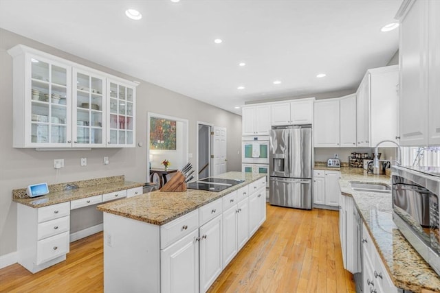 kitchen featuring black electric cooktop, stainless steel refrigerator with ice dispenser, a kitchen island, a sink, and light wood-style flooring