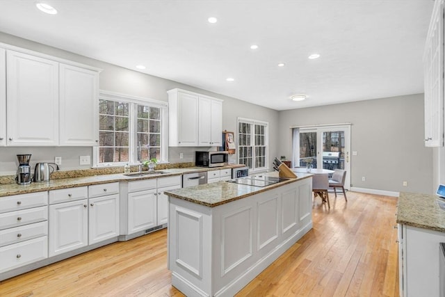kitchen featuring a sink, a kitchen island, black electric cooktop, stainless steel microwave, and white cabinets