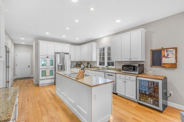 kitchen featuring a kitchen island, appliances with stainless steel finishes, beverage cooler, light wood-style flooring, and white cabinets