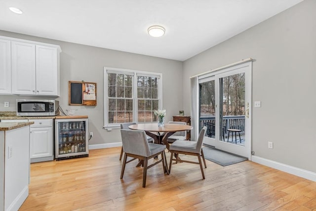 dining room with baseboards, wine cooler, and light wood-style floors