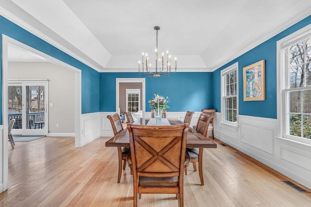 dining space featuring light wood-style flooring, a tray ceiling, visible vents, and a notable chandelier