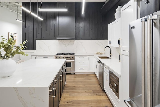 kitchen with backsplash, white cabinets, sink, light hardwood / wood-style flooring, and premium appliances